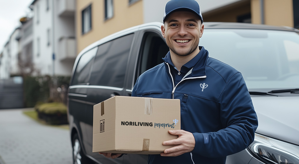 Lächelnder Lieferbote mit Paket vor Lieferwagen Ein Lieferbote in blauer Uniform hält ein Paket vor einem Lieferwagen in einer Wohngegend.